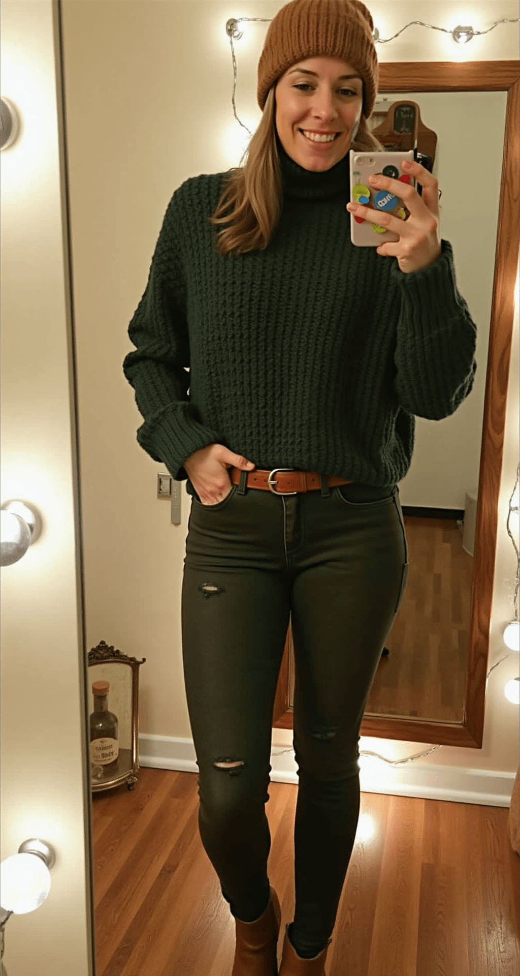 Cozy dressing area with string lights featuring a person in a black turtleneck under a forest green chunky sweater, tucked into high-waisted dark denim; cinched with a cognac leather belt, complemented by a matching beanie and ankle boots. Mirror reflects various styling techniques amidst soft, warm lighting highlighting layered textures.