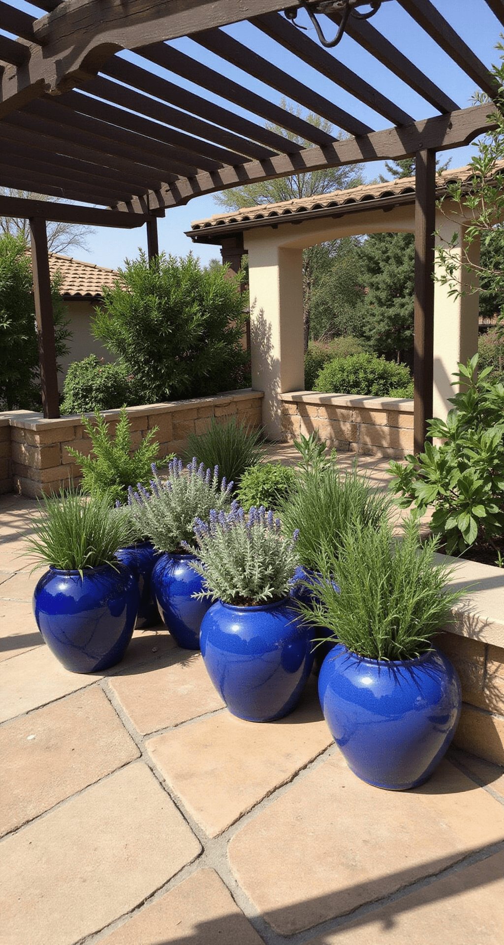 A Mediterranean-inspired patio herb garden featuring blue glazed ceramic containers arranged in a symmetrical pattern on a stone terrace. The garden includes drought-tolerant herbs like sage, rosemary, and lavender, with sunlight filtered through a pergola casting striped shadows. The scene showcases a color palette of cobalt blue, silvery foliage, warm sandstone, and deep shadows.