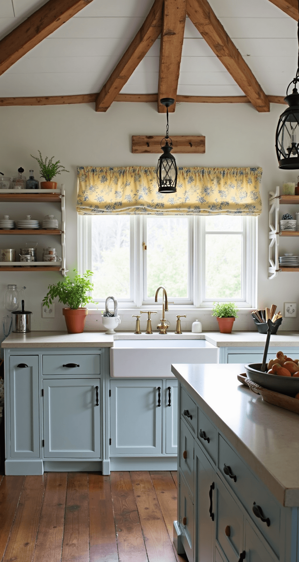 A cozy farmhouse-style kitchen featuring pale gray-blue cabinets, rustic wooden beams along the ceiling, and natural light filtering through cafe curtains. The soapstone countertops and white apron sink enhance the authentic feel, complemented by antique brass hardware and lantern pendants. Vintage accessories, an enamelware collection, and fresh herbs in terra cotta pots add lived-in charm, with morning light highlighting the cabinet color variation.