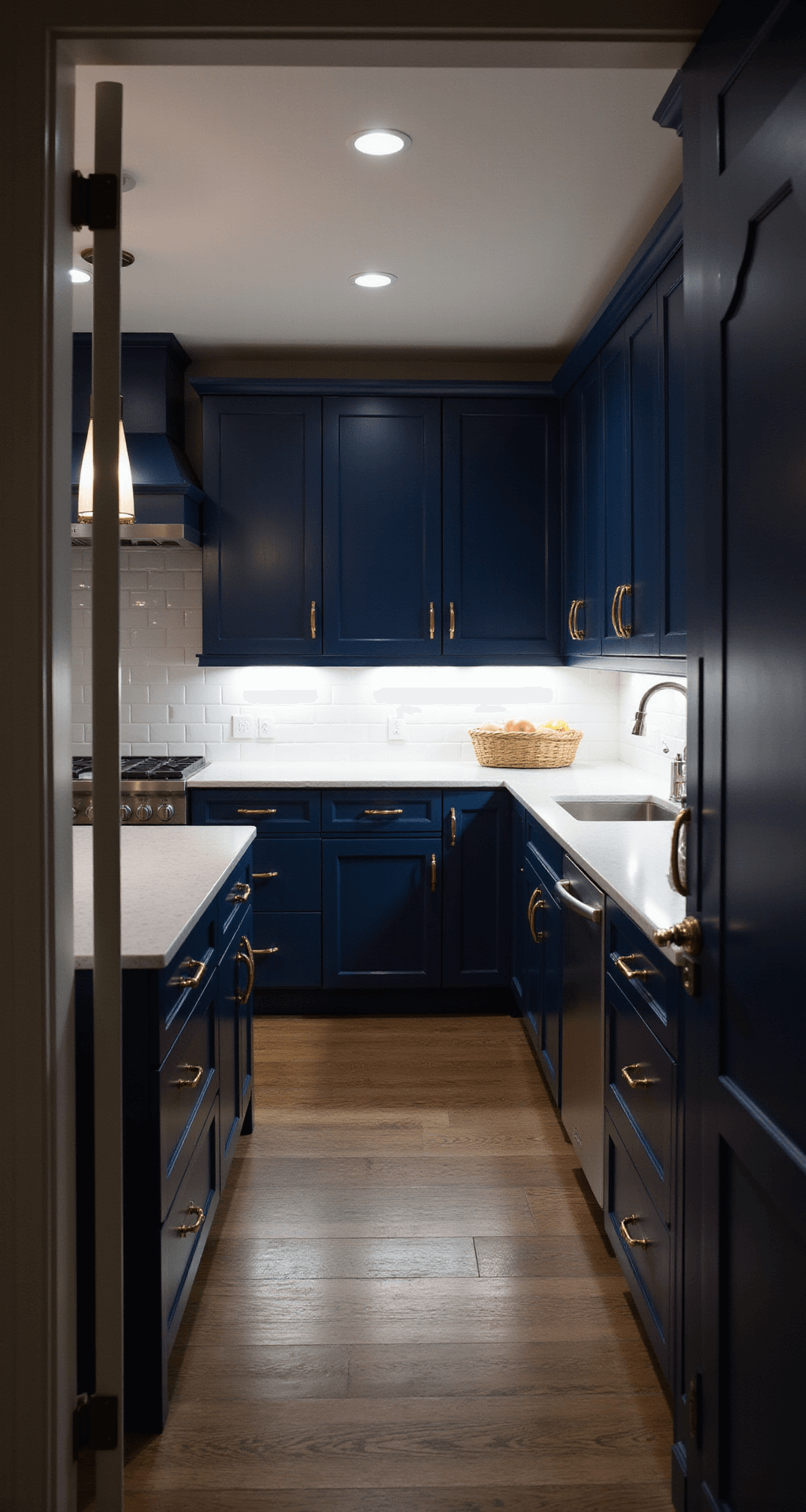 Dramatic evening kitchen scene featuring navy blue cabinets with brushed nickel hardware, white subway tile backsplash, and illuminated under-cabinet LEDs, viewed from the doorway at eye level, highlighting a moody atmosphere.