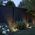 Photorealistic twilight garden scene showcasing a tall matte black horizontal slat fence, illuminated by LED uplighting, framed by white David Austin roses and silver-leafed artemisia, with a blurred background and ethereal lighting effects.