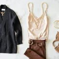 Overhead shot of a layered outfit on a white marble surface, featuring a silk camisole, chunky knit sweater, leather pants, gold jewelry, structured handbag, and suede ankle boots, with soft natural lighting and a clean white background.