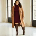 Plus-size model in a cozy urban studio wearing a camel wool peacoat over a burgundy turtleneck sweater dress, paired with brown leather boots, showcasing elegant winter fashion with warm natural lighting and minimalist decor.