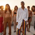 A diverse group of models on a rooftop during golden hour, featuring a central model in a white oversized shirt and rainbow-striped wide-leg pants, with the city skyline in the background, capturing a dreamy, warm atmosphere and showcasing pride fashion elements.