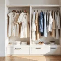 A bright, minimalist walk-in closet with a curated spring capsule wardrobe in neutral tones, featuring cream jumpsuits, oatmeal cardigans, and light denim, complemented by gold jewelry and silk scarves, illuminated by natural sunlight.