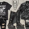 Flat lay of edgy concert attire on a concrete background, featuring a distressed vintage band tee, ripped black jeans, a worn leather jacket, combat boots with metal hardware, layered silver chains and chokers, a studded belt, and a leather crossbody bag, with natural sunlight creating subtle shadows.