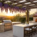 Luxurious outdoor kitchen under a cedar pergola at sunset, featuring Mediterranean cream stone countertops, stainless steel grill, wisteria vines, quartz island with ivory seating, and artisanal pizza oven, set in a manicured garden with warm lighting and natural lens flare.
