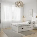 A bright Scandinavian-style bedroom featuring a white MALM bed, floating nightstands, and floor-to-ceiling shelving units, illuminated by natural light through sheer curtains, with a minimalist decor of a monstera plant and neutral bedding.