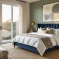 A luxurious master bedroom with a navy velvet tufted headboard, sage green accent wall, and crisp white linens, featuring mid-century modern furniture, oversized abstract artwork, and natural elements like a fiddle leaf fig. The scene is illuminated by golden hour sunlight through floor-to-ceiling windows, showcasing rich textures and a hyper-realistic photographic style.