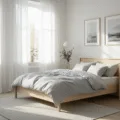 A minimalist Scandinavian bedroom featuring a MALM bed frame with light grey and white bedding, bathed in morning sunlight with sheer white curtains, showcasing natural wood accents and curated decor.