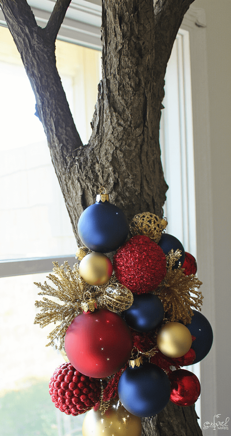 Dramatic vignette of a tree's mid-section adorned with a collection of mixed ornaments, including navy mercury glass balls, crimson matte spheres, and antiqued gold accents, captured with natural light highlighting sparkle points on glossy surfaces.